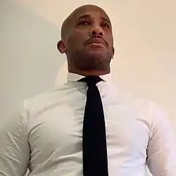 A headshot of Soufiane Sankhon taken from below, he is wearing a white shirt with a black tie