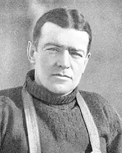 Head and shoulders of a dark-haired man looking directly to camers. The straps of a harness over his shoulders are visible.