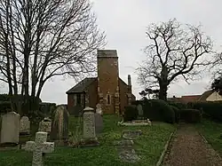 A simple church with a square tower, seen in a graveyard with tombstones and with trees silhouetted against the sky