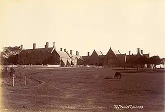 Early 20th century photo of college buildings, with horse grazing in pasture in foreground