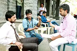 Sudeepa and Nani sit in chairs and listen to Rajamouli.