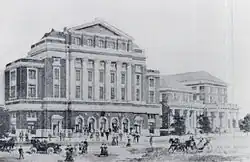 An artistic rendering of the building as built, with two other buildings next to it and people around.