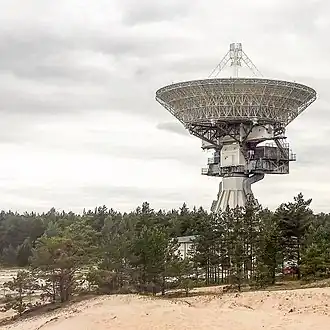 A large radio dish is facing upward towering above the trees