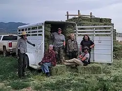 A group of people pose for a photo in a field, in and around a trailer with hay bales