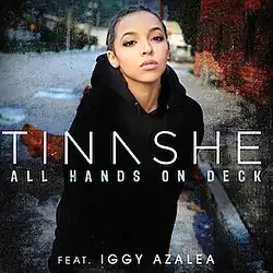 A portrait of a young African-American woman posing on a street sidewalk in a black coat. Centered in white font is the name, Tinashe, and below it, the title "All Hands on Deck", with "Feat. Iggy Azalea" underneath it.