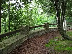 A trail in a forested area with a rock and wood wall.