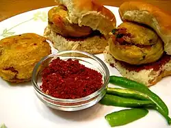 One batata (potato) vada, two vada pavs, raw green chillies, and seasoning of red garlic chutney.