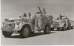 vehicles in convoy, each crewed by three men, in a desert terrain