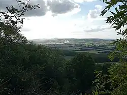 19th-century painting of a hilly landscape, sen from a hill with trees framing the view