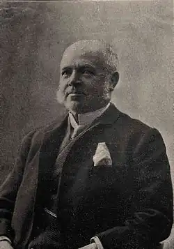 An old man with white hair and sideburns wearing a suit