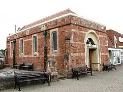 Rectangular church like building in red brick with contrasting natural light stone features, high windows and high arched entrance against a light sky