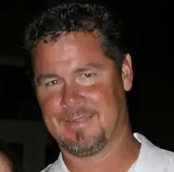 A smiling man with short curly hair and a salt-and-pepper goatee