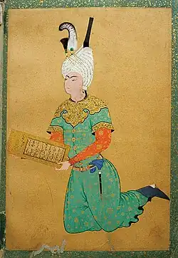 A youth with a turban kneeling and holding a piece of ornated paper