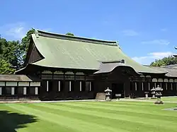 Wooden building with a hip-and-gable roof and attached canopy with Chinese style gable. On either side, the building is connected to a wooden corridor.